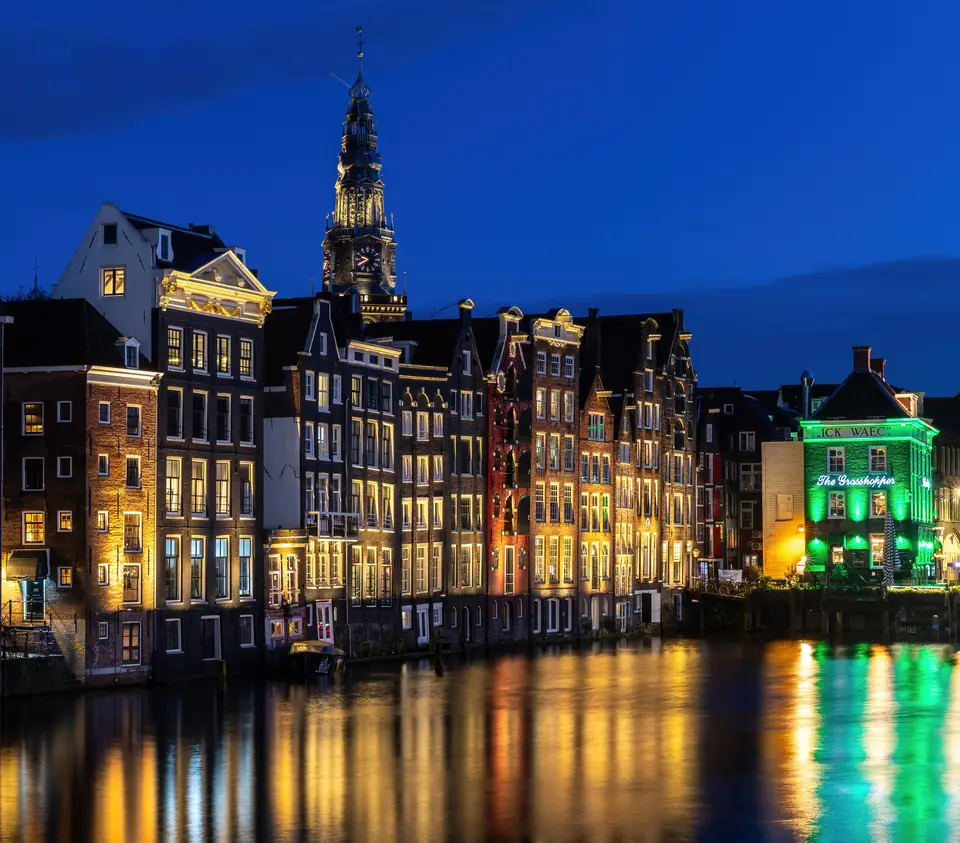 Casas de canal en Ámsterdam de noche, con la torre de la Oude Kerk al fondo, reflejadas en el agua