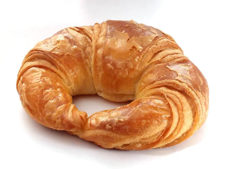 Croissant clásico de hojaldre entero sobre fondo blanco