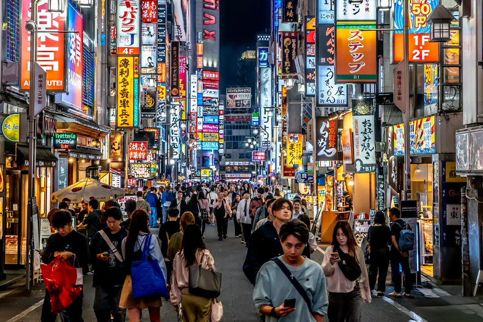 Calle de Shinjuku con carteles de neón y gente caminando de noche, Tokio